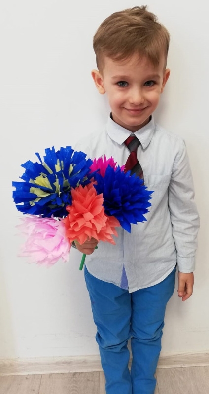 Chłopiec w eleganckiej koszuli trzyma kwiaty z bibuły.