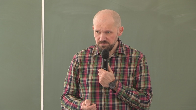 Meżczyzna w koszuli w kratę trzyma mikrofon.