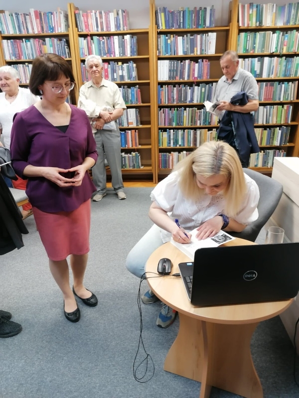 Autorka siedzi na krześle i podpisuje książki