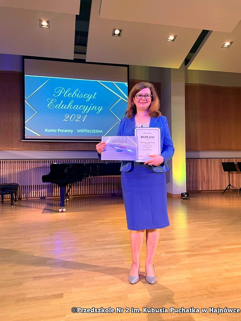 Kobieta w niebieskiej garsonce trzyma dyplom i voucher.