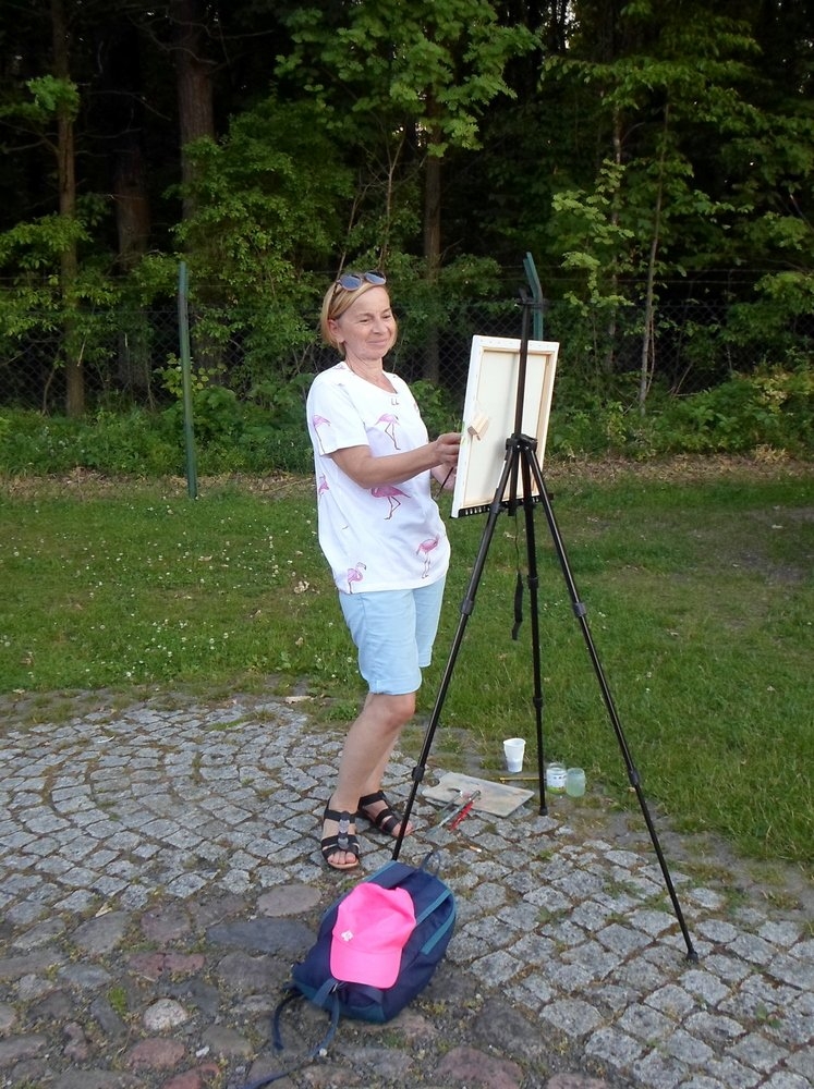 Kobieta stoi przy sztaludze i maluje.