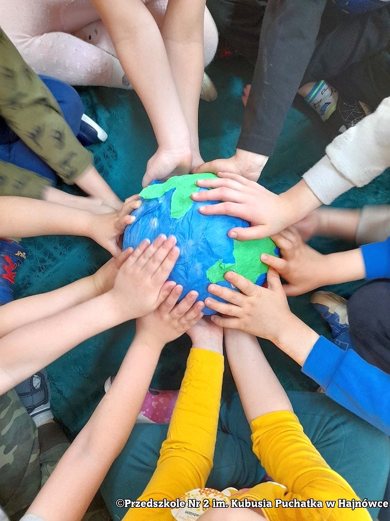 ręce dzieci dotykające kulę ziemską wykonaną z materiałów plastycznych.