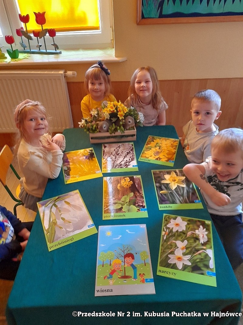 Sześcioro dzieci sziedzi przystoliku, na stole leżą fotografie kwiatów.