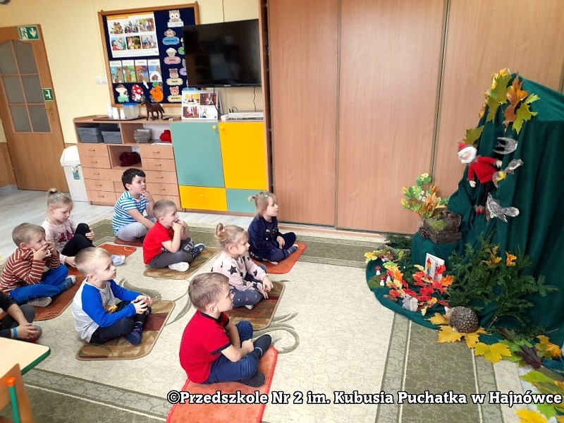 Dzieci siedzą na podłodze i oglądają spektakl.