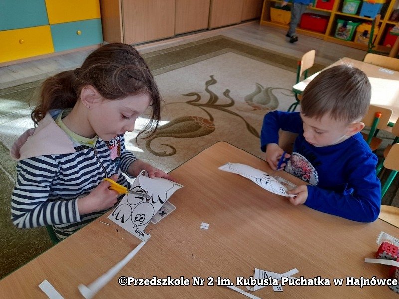 Dzieci siedzą przy stolikach i wycinają.