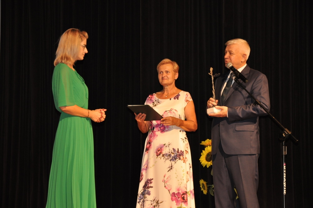 Burmistrz Miasta wręcza statuetkę Marcie Gredel - Iwaniuk, kobieta ubrana jest w dłogą, zuekoną sukienkę.