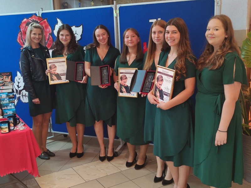 Siedem dziewczyn stoi i pozuje do zdjęcia, część z nich trzyma dyplomy.