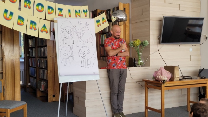 Tomasz Samojlik stoi przy tablicy z rysunkami Pompika.