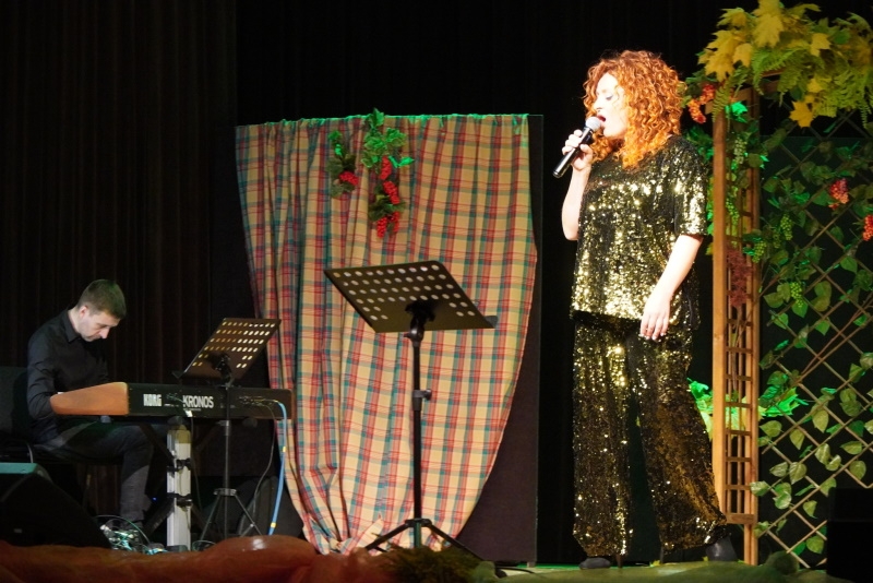 Kobieta w zielonym błyszczącym stroju śpiewa do mikrofonu.