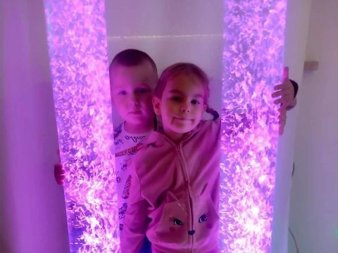 Zdjęcie przedstawia dwoje dzieci stojących obok siebie pomiędzy dwoma słupami świetlnymi.