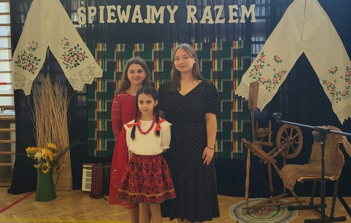 Trzy dziewczynki. W tle widać tematyczną, regionalną scenografię.