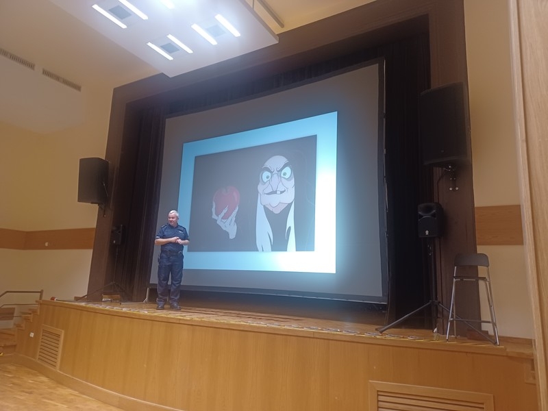 Na scenie stoi policjant, za którym na dużym ekranie wyśwtlany jest obraz z bajki.