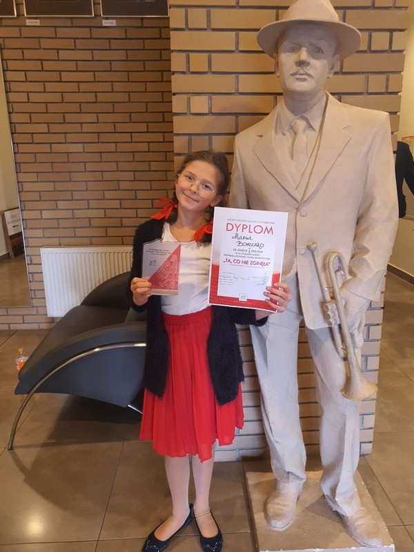 dziewczynka z dyplomem przy posągu meżczyzny