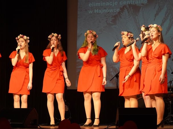 sześć dziewcząt w czerwonych sukienkach stoi na scenie