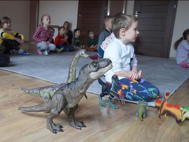 dzieci oglądają bajkę, obok ustawione są zabawki - dinozaury