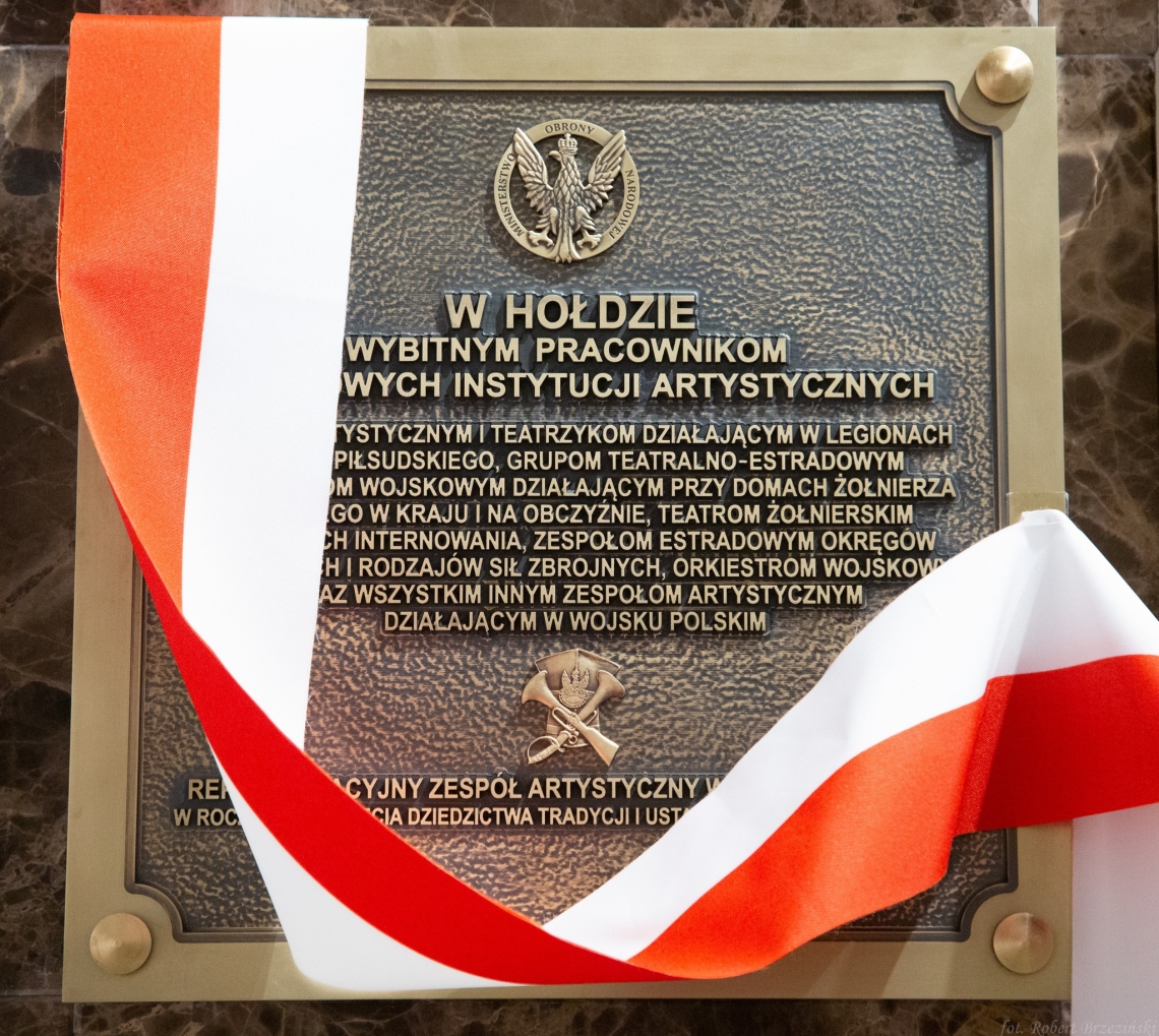 tablica pamiątkowa wykonana w brązie, przez nią przewieszona jest biało-czerwona wstęga