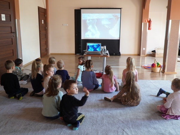 Dzieci siedzą na dywanie i oglądają film.