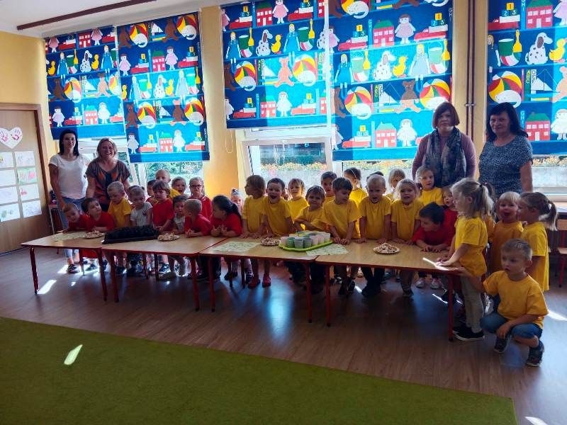 Dzieci wraz z nauczycielkami stoją przy stole przygotowanym do poczęstunku.
