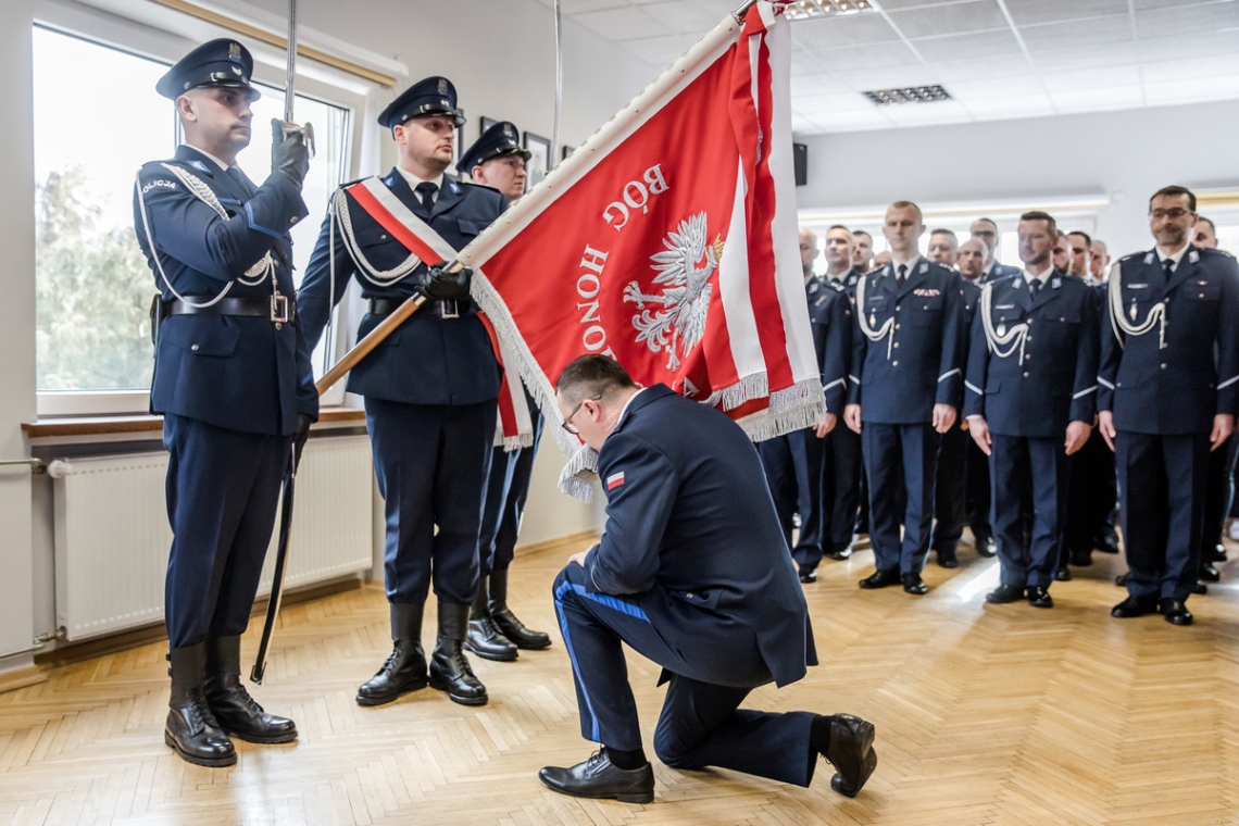 mężczyzna w mundurze klęka przed sztandarem