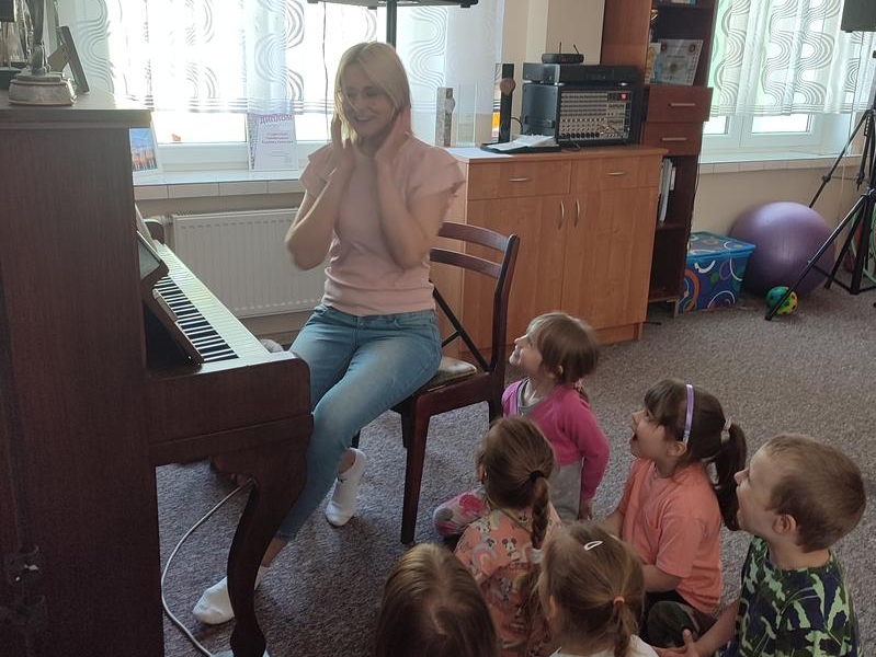 kobieta przy pianinie pokazuje dzeciom ćwiczenie