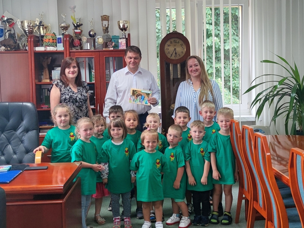 grupa dzieci w zielonych koszulkach pozują do zdjecia z opiekunkami i burmistrzem w gabinecie Burmistrza Miasta Hajnówka