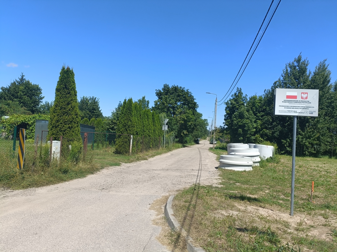 zdjęcie trwajacej inwestycji drogowej wraz z tablicą informacyjną o dofinansowaniu
