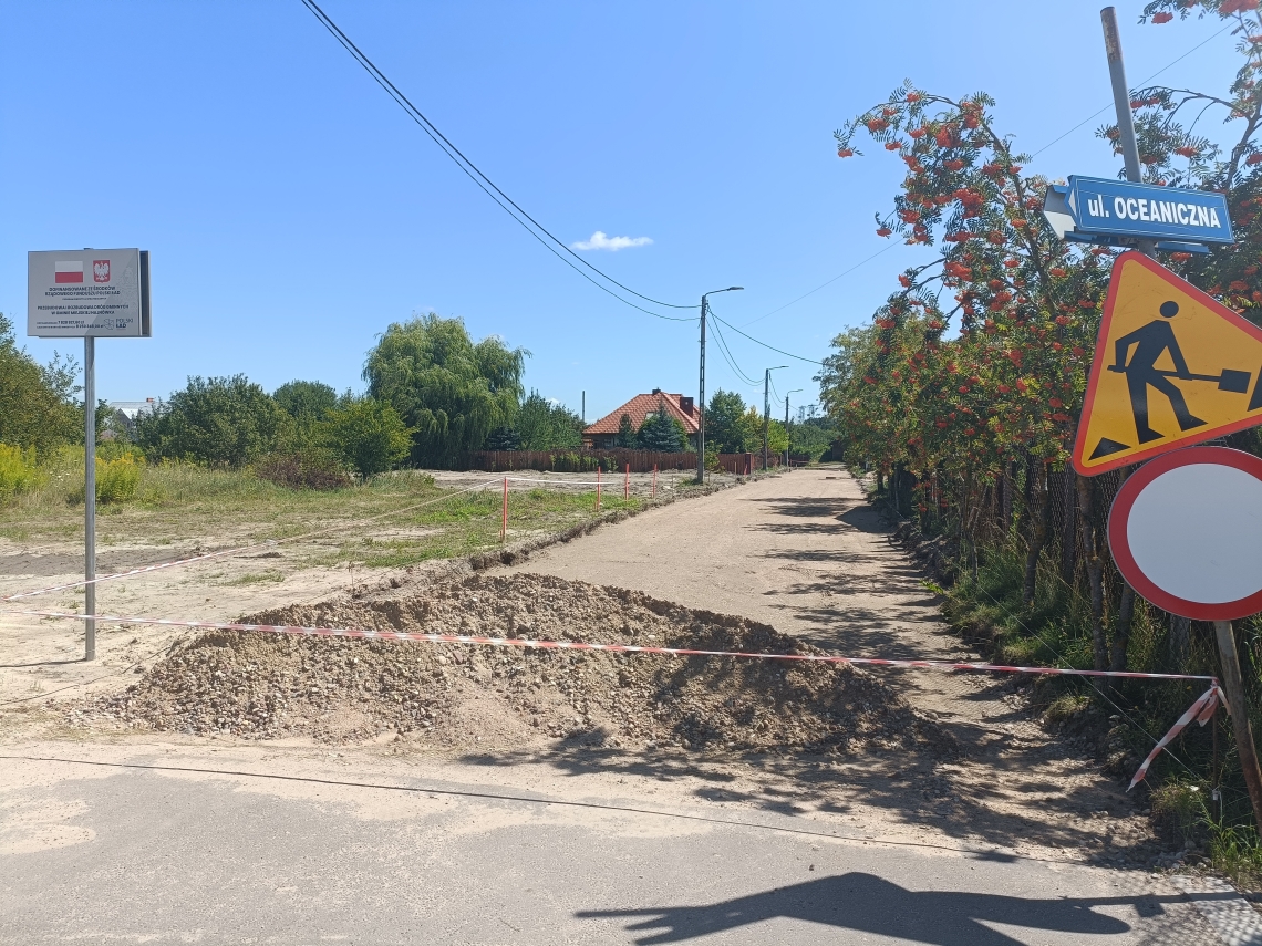 zdjęcie trwajacej inwestycji drogowej wraz z tablicą informacyjną o dofinansowaniu