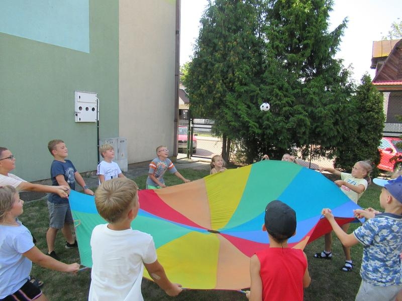 Grupa dzieci bawi się chustą animacyjną.