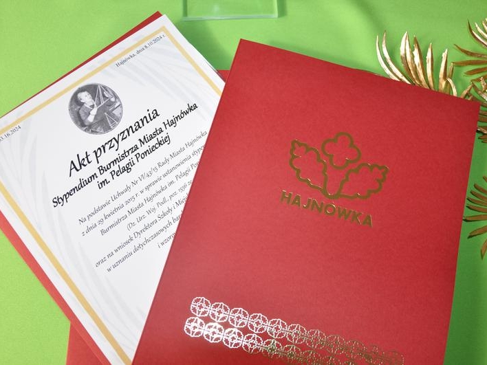 akt nadania stypendium w czerwonych okładkach z logo Miasta Hajnówka