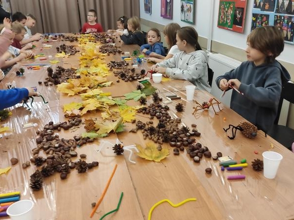 dzieci siedzą przy stole, na którym leżą kasztany i liście