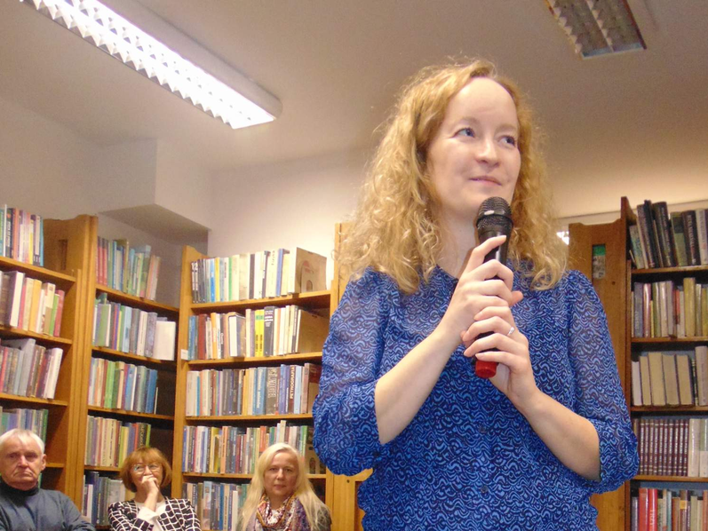 kobieta trzyma miktrofon. W tle widać regały z książkami