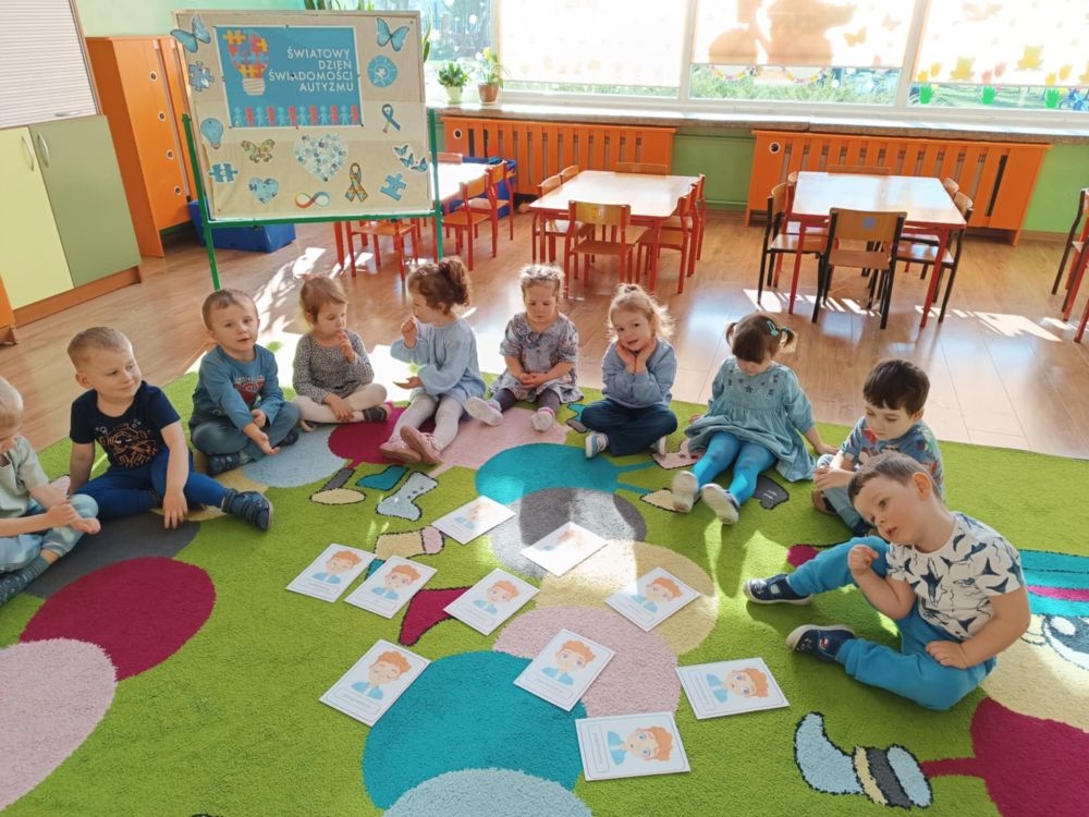 dzieci siedzą na dywanie i pracują z kartami pracy