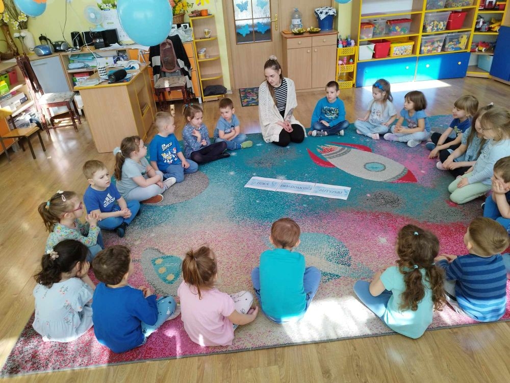 dzieci siedzą na dywanie i pracują z kartami pracy