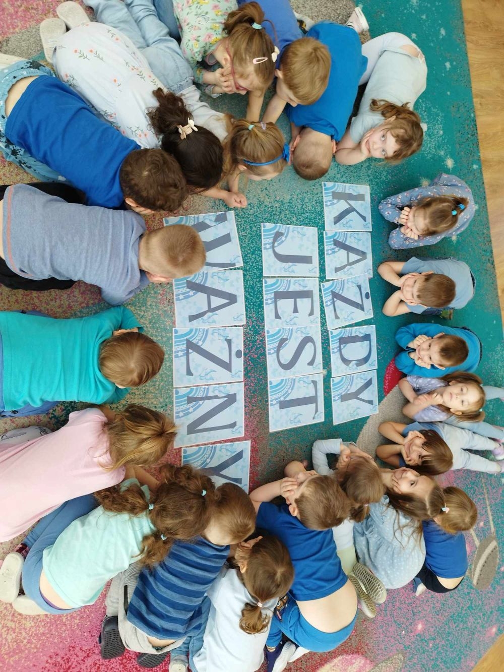 dzieci siedzą na dywanie i pracują z kartami pracy