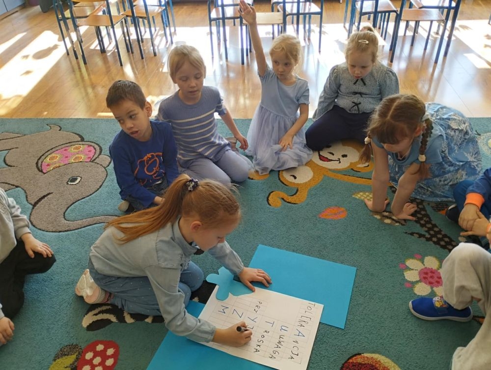 dzieci siedzą na dywanie i pracują z kartami pracy