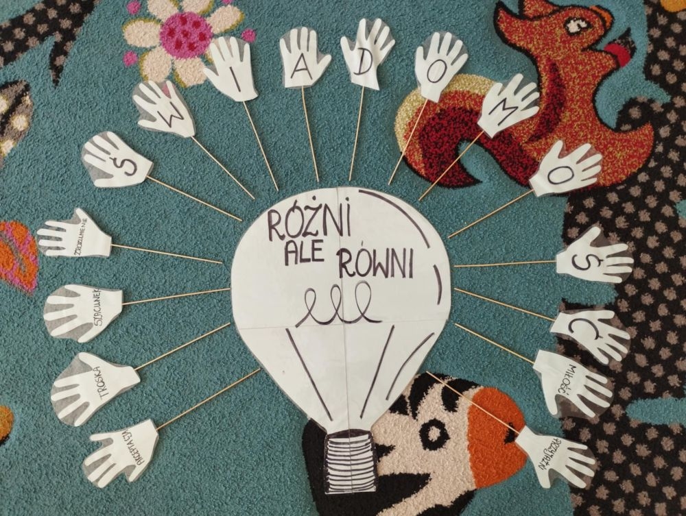 dzieci siedzą na dywanie i pracują z kartami pracy