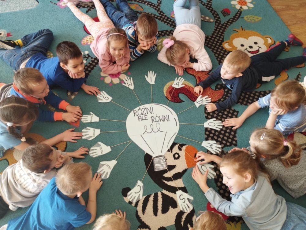 dzieci siedzą na dywanie i pracują z kartami pracy