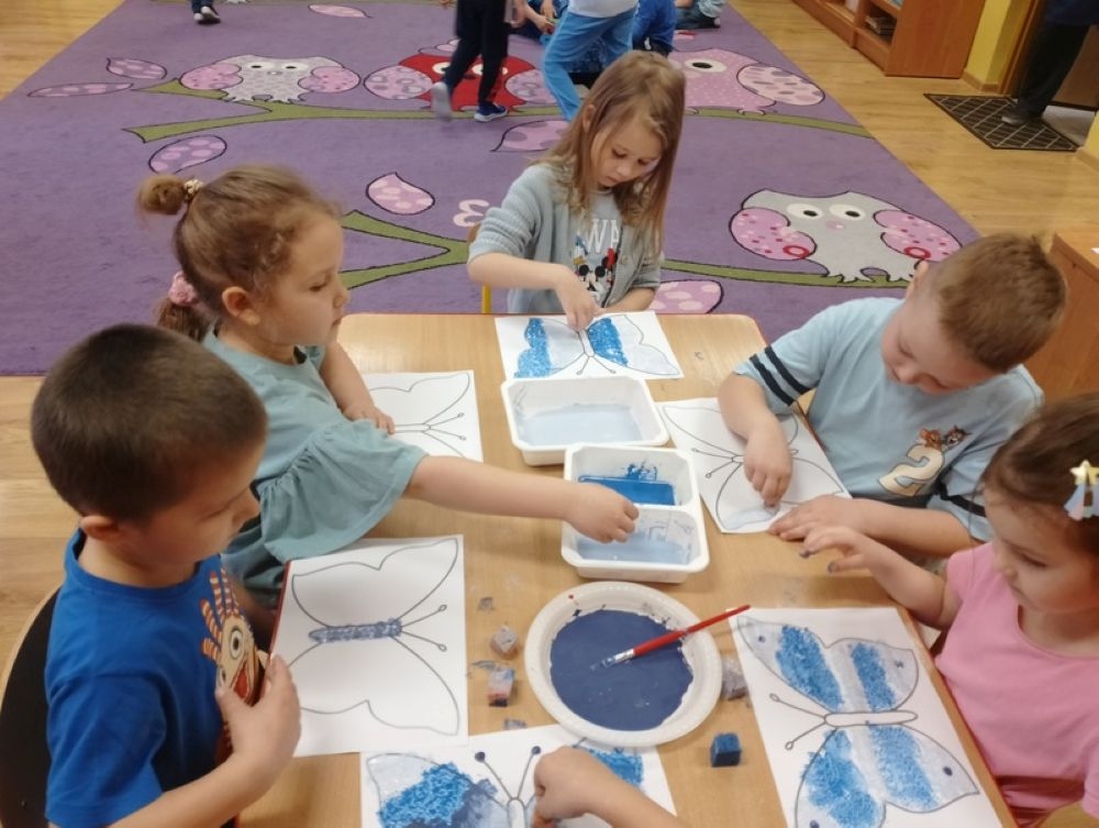 dzieci siedzą na dywanie i pracują z kartami pracy