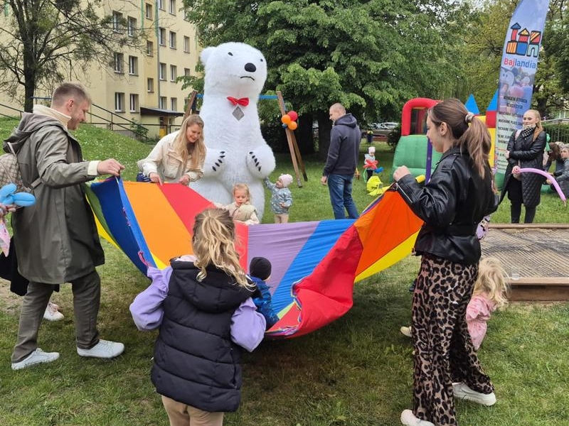 dzieci i rodzice podczas zabawy na pikniku. W tle widać maskotę dużego misia