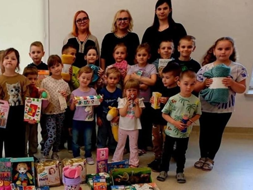 grupa dzieci z panią dyrektor i nauczycielkami. Dzieci trzmyjaą zabawki i gry