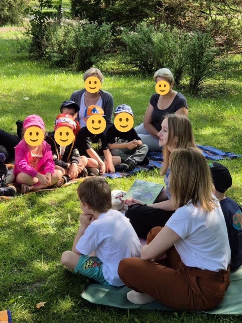 dzieci siedzą na trawie i słuchają opowieści