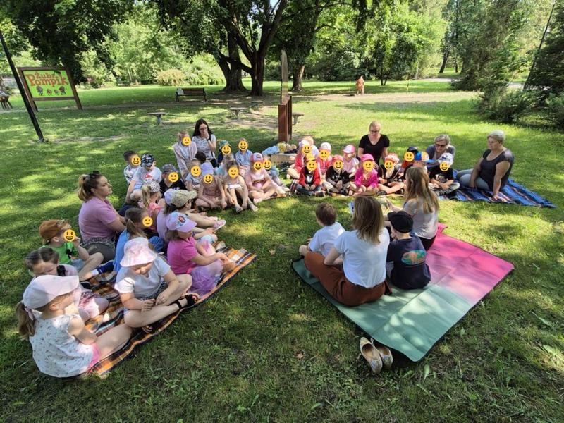 dzieci siedzą na trawie i słuchają opowieści