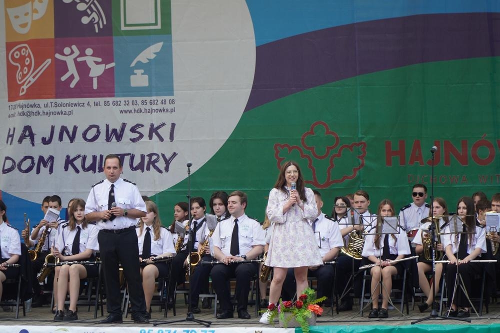 kobieta przy mikrofonie, w tle widać orkiestrę dętą