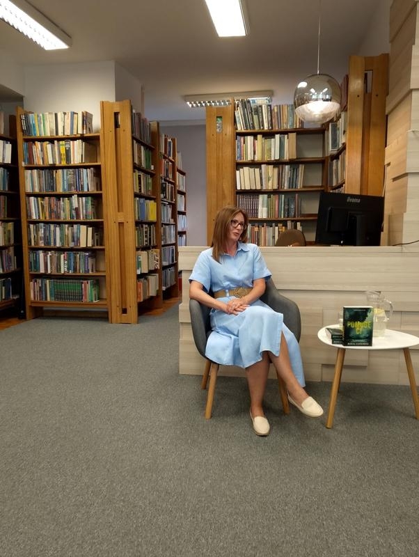 kobieta siedzi przy stoliku, w tle widać półki z książkami