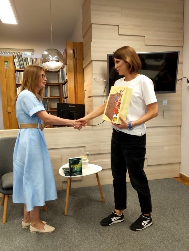 dwie kobiety podają sobie dłonie. Jedna trzyma torbę z podarunkiem