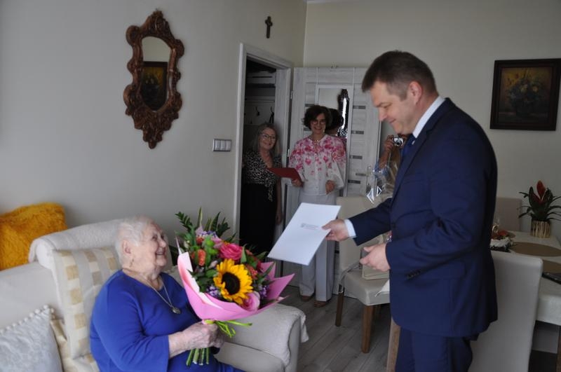burmistrz wręcza Jubilatce dyplomy, w tle widać panią kierownik USC i członków rodziny
