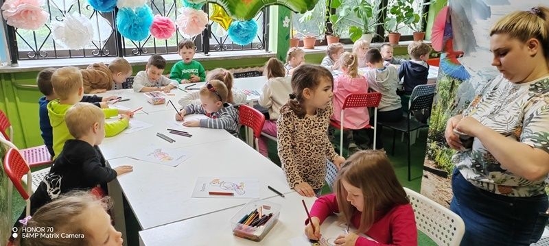 dzieci kolorują przy stolikach obrazki z papugami