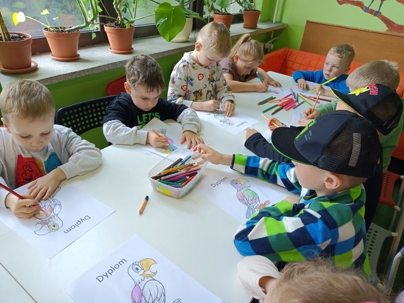 dzieci kolorują przy stolikach obrazki z papugami