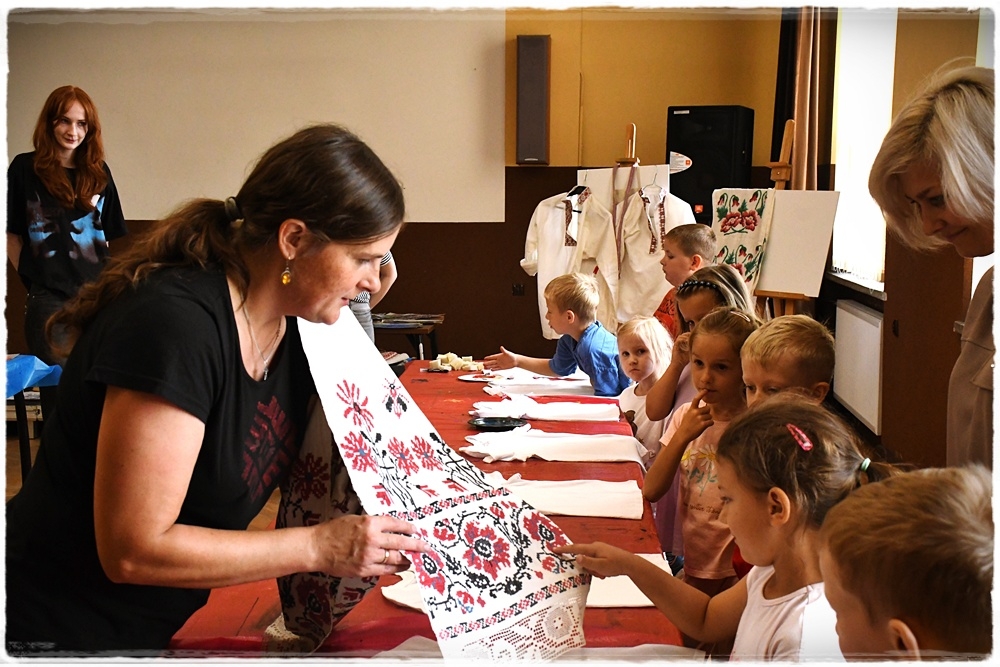 pracownik muzeum pokazuje dzieciom wyszywane ręczniki ludowe