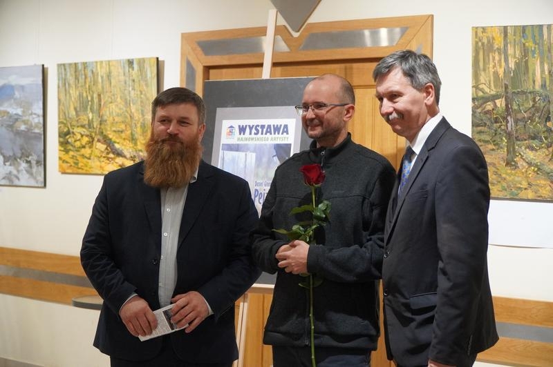 trzej mężczyźni pozują do zdjecia. W tle wystawa.